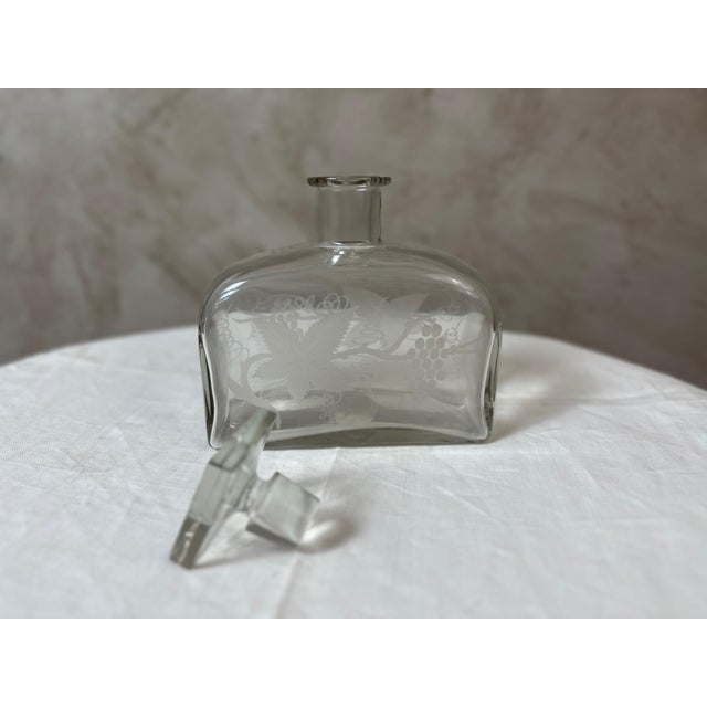 An elegant glass decanter dating from the 1940s, adorned with a delicate engraved design of vine leaves, bunches of...