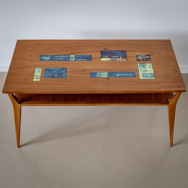 Coffee table on conical legs with a rectangular table top. The table top is inlaid with colorful glazed ceramic discs in...