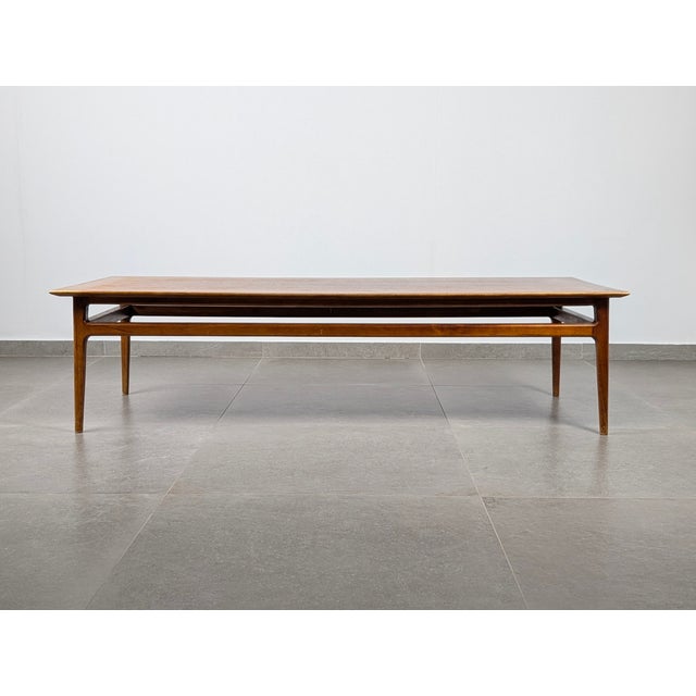 Crafted from deep, warm-toned teak, this large coffee table embodies the refined elegance of 1950s Scandinavian Modern....