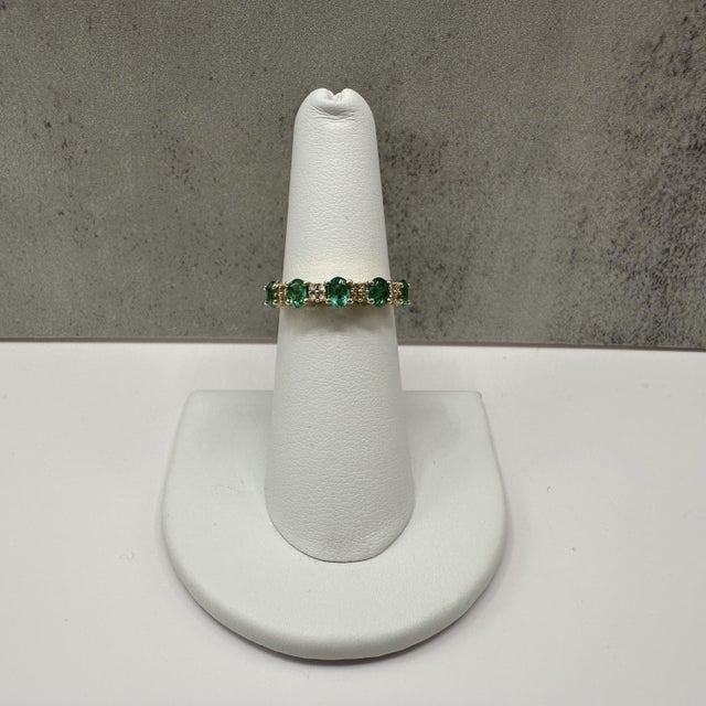 This emerald and diamond ring is crafted in 10kt yellow gold and features five vibrant 4x3mm oval cut green emeralds...