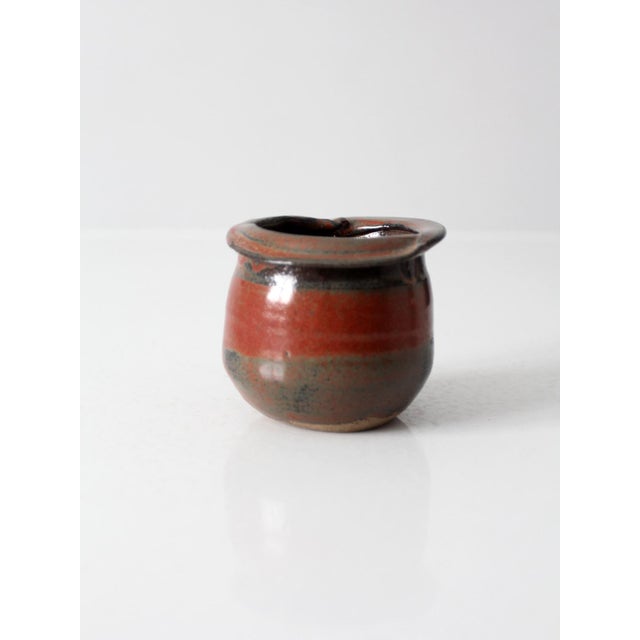 Vintage handmade studio pottery vessel featuring a rounded form, softly flared rim, and a rich red and charcoal glaze. The...
