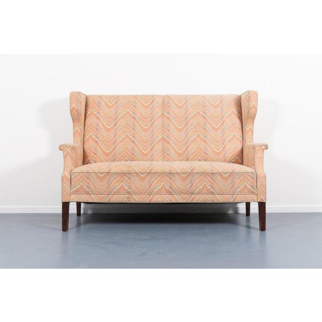 Very beautiful imposing wingback wall sofa on stained wood legs with spectacular colorful fabric upholstery. Produced in...