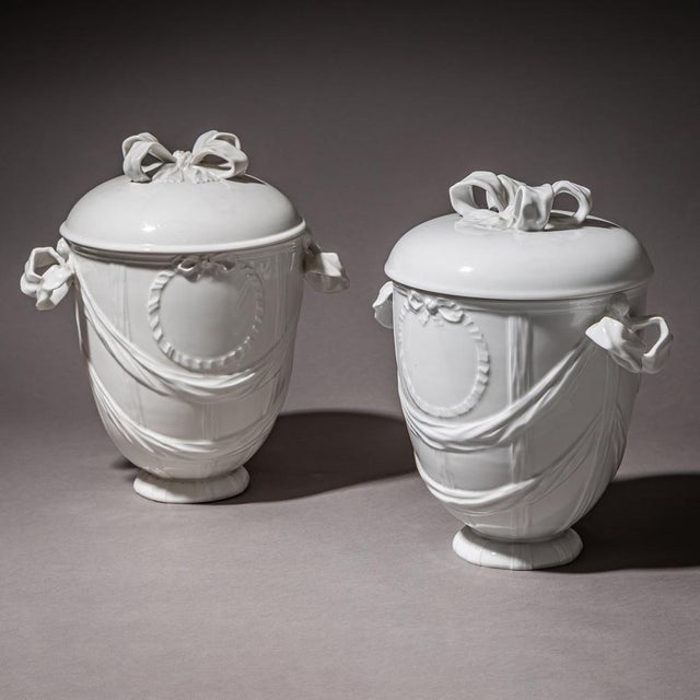 Pair of lidded urns in white-glazed porcelain by KPM Berlin, with ribbon handles and draped festoons on the body. The...