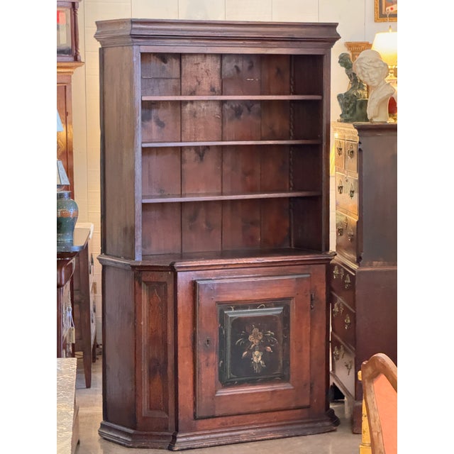 Tall Swedish cabinet with molded crown, open upper shelves, and a single lower door with a floral painted panel. The worn...
