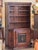 Tall Swedish cabinet with molded crown, open upper shelves, and a single lower door with a floral painted panel. The worn...