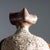Anthropomorphic terracotta sculpture with a bulbous body and long arms. The hands are interlocked and the wedge-shaped...