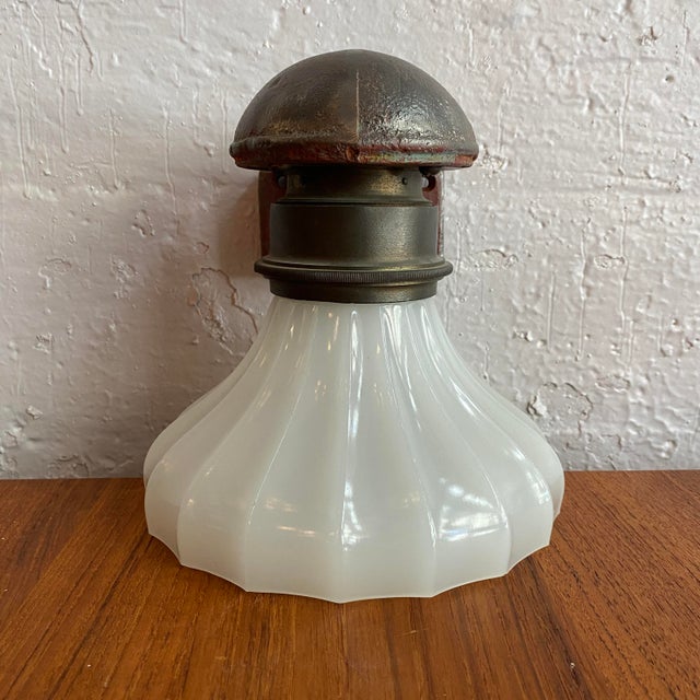 This early 20th-century industrial wall sconce features a heavy, architectural cast iron wall mount with a textured...
