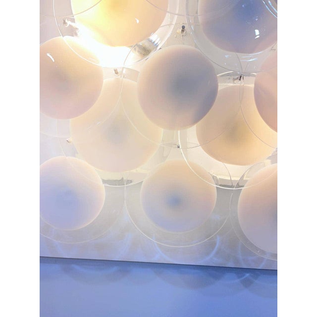 Nine mouth-blown glass discs, each featuring a satin-white opaline core encircled by a ring of clear crystal, form the...