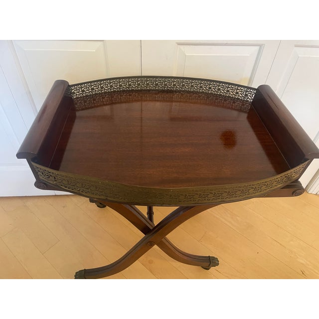 Listed is a vintage wooden folding serving tray table featuring a rich, dark wood finish, decorative metal gallery sides,...