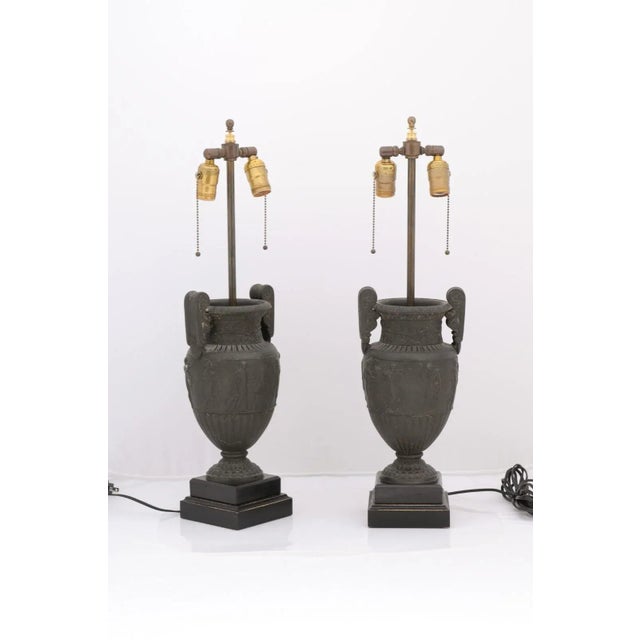 These basalt black urns are mounted on onyx and enameled wooden bases. The grecian mural on each is complimented by laurel...