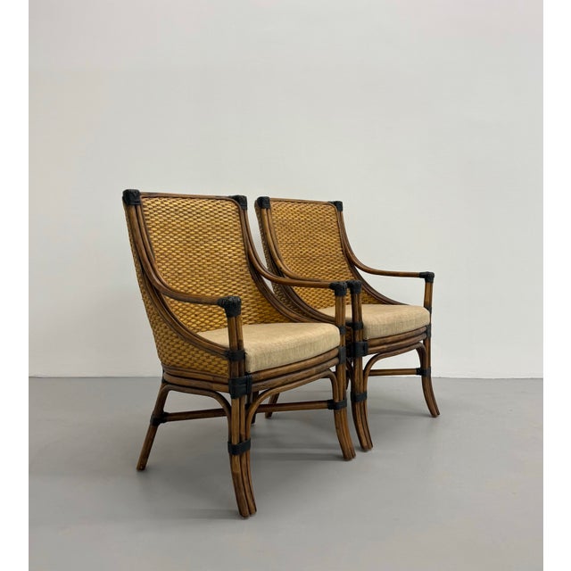 A sophisticated pair of vintage lounge chairs crafted with a curved rattan frame, tightly woven backs, and contrasting...