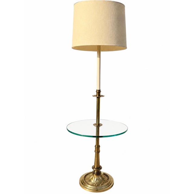 Elegant vintage brass floor lamp featuring a sculptural pedestal base with ornate floral detailing, accented by a circular...