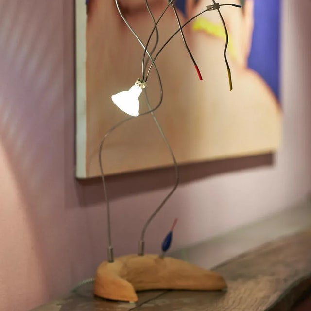 Table light characterized by exposed cables. The light source is connected to the central body through thin colored steel...