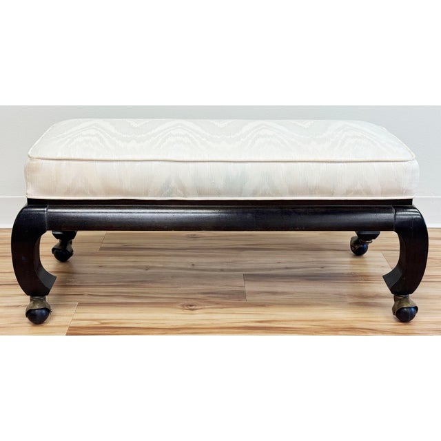 Vintage ebonized carved wood Ming style bench or footstool on casters. Original ivory upholstery is piped at edges for a...