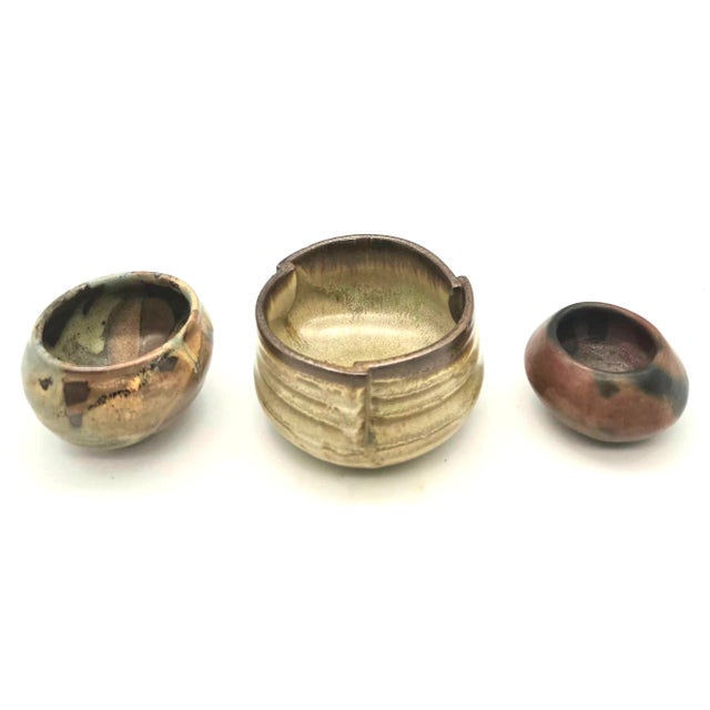 Offered are 3 artisan-crafted small studio pottery vessels or Japanese-style round tea bowls (chawan) featuring earth-...