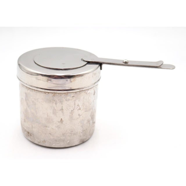 Chafing dish fuel holder made of brass with a silver finish featuring a flapper top and a long handle. Made by D.W. Haber...