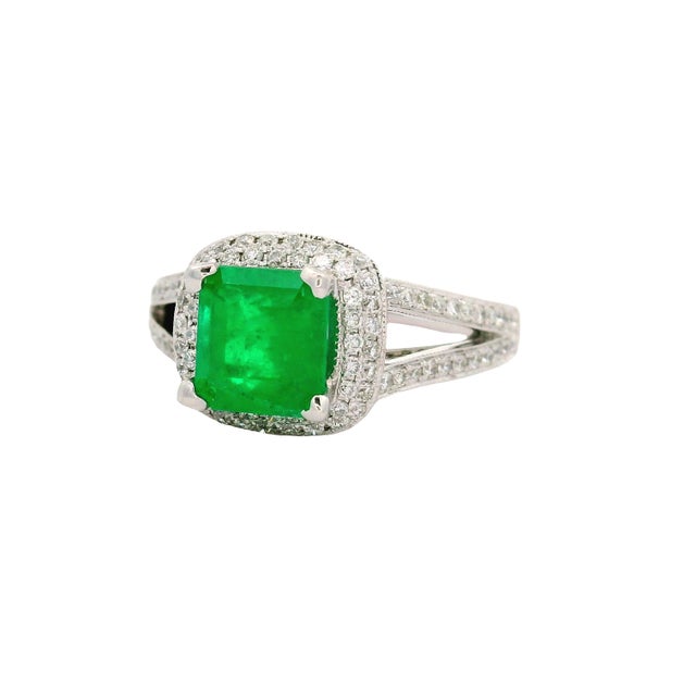 This elegant ring features a vibrant, emerald-cut emerald from Colombia as its centerpiece, securely held by four elegant...