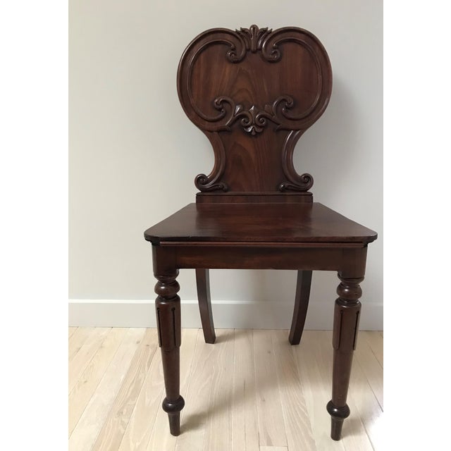 Antique hall chair with dramatic and intricate carving. Solid seat and back with double c-scroll details and fleur-de-lis...