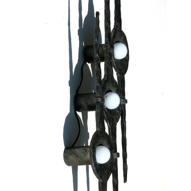 This Brutalist wall lamp in wrought iron was produced in the 1960s. It remains in working order. European Plug (up to...