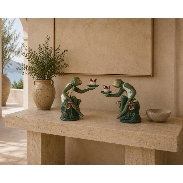 A whimsical and highly decorative pair of vintage Chinoiserie monkey candleholders, modeled as seated monkeys presenting...