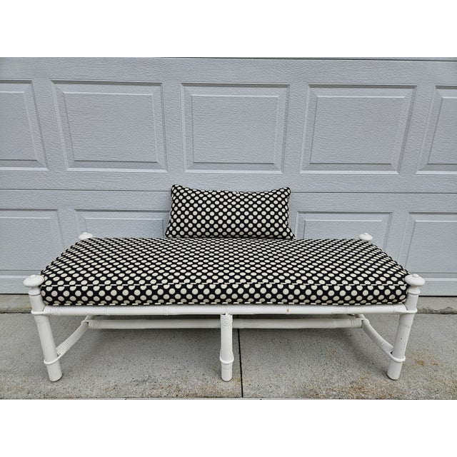 This vintage reed and bamboo upholstered bench is white and has a fitted upholstered seat cushion. The upholstery is black...