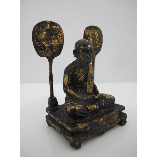 Antique Thai bronze figurine depicting a seated monk with flanking ceremonial fans painted in light gold leaf...