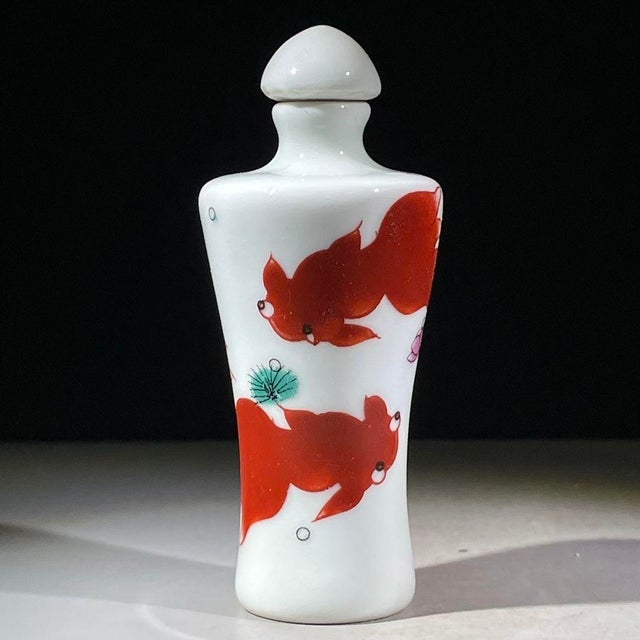 A charming Chinese porcelain snuff bottle with a matching lid. The white ground is hand-painted in vibrant iron red...