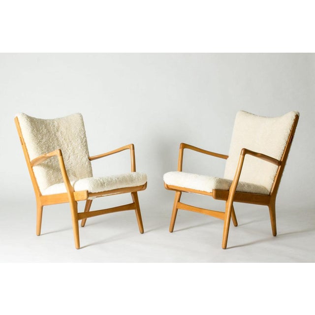 Pair of elegant and comfortable “AP 16” lounge chairs by Hans J. Wegner. Made from oak and upholstered with cosy sheepskin.