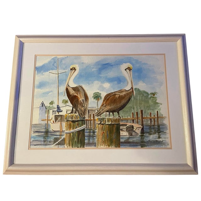 Large framed watercolor depicting two pelicans perched along a dock with boats and palms in the background. Strong coastal...