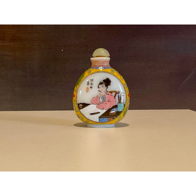 Elegant Famille Rose porcelain snuff bottle featuring finely hand‑painted floral and figural motifs in soft rose, emerald,...