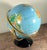 Vintage world globe on a gold-tone metal stand with black lacquered base, featuring a vibrant multi color surface and...