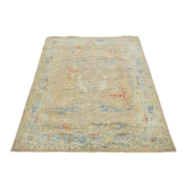 This hand-knotted wool rug has a light brown background and blue frame adorned with multicolor all-over designs. This rug...