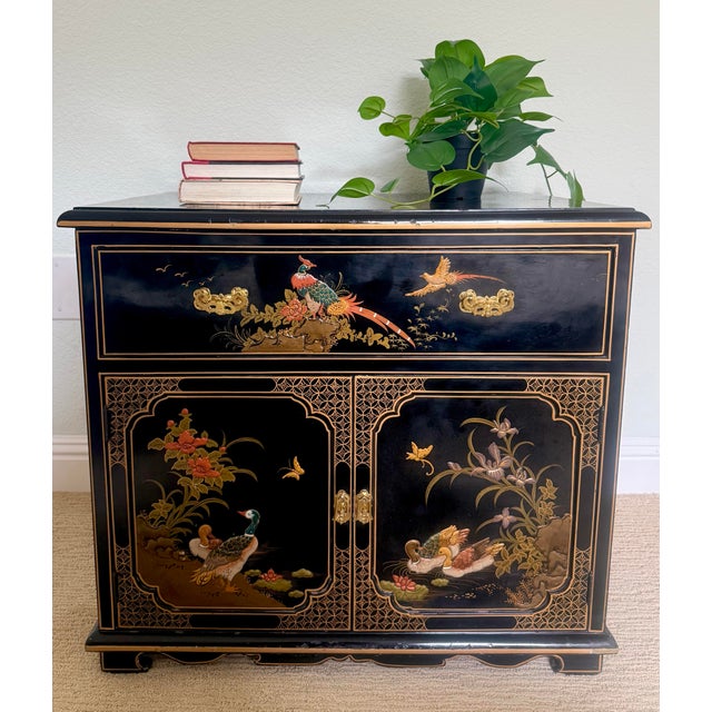 A beautifully restored vintage chinoiserie cabinet, likely dating to the late 20th century, featuring a classic black...