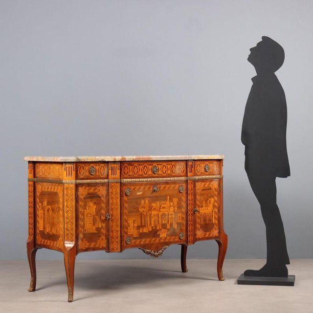 Napoleon III-style chest of drawers, richly inlaid with various woods. It features a curved front with a slightly...