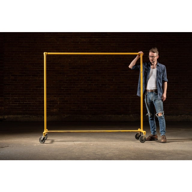 Yellow industrial garment rack on casters. Constructed from painted steel pipe with threaded joints, this utilitarian...