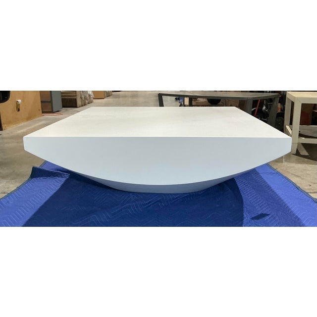 This sculptural white cocktail table features a bold contemporary design with a clean square top and softly rounded...
