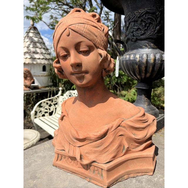 A charming French-style terracotta bust depicting an elegant young woman in romantic Art Nouveau-inspired dress. The...