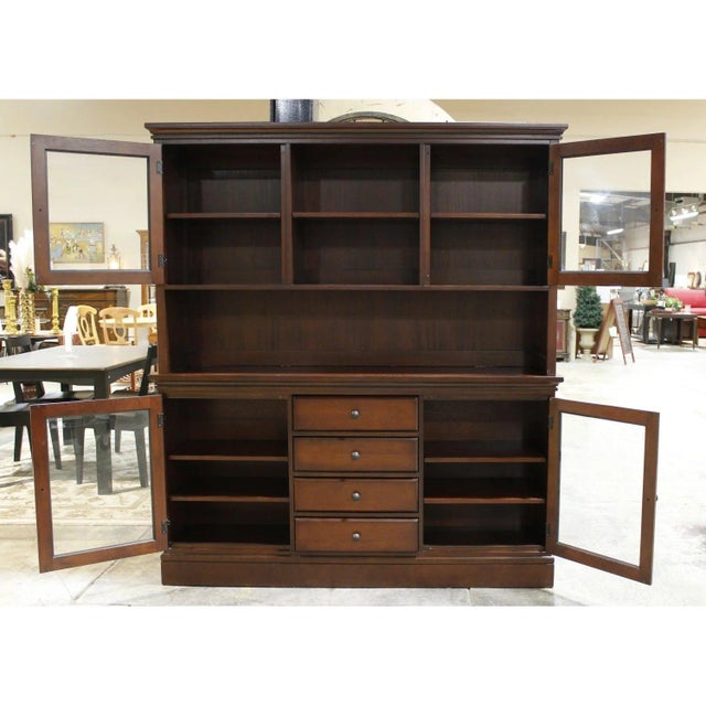 Finished in a dark brown wood tone, this traditional-style piece features four glass-paneled cabinet doors with interior...