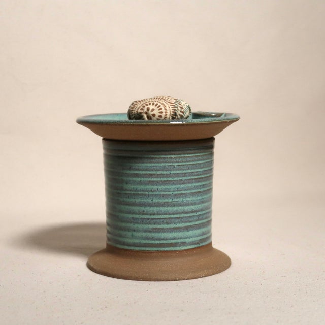 A charming handmade ceramic pin cushion jar featuring a soft turquoise glaze over ribbed stoneware with a natural clay...