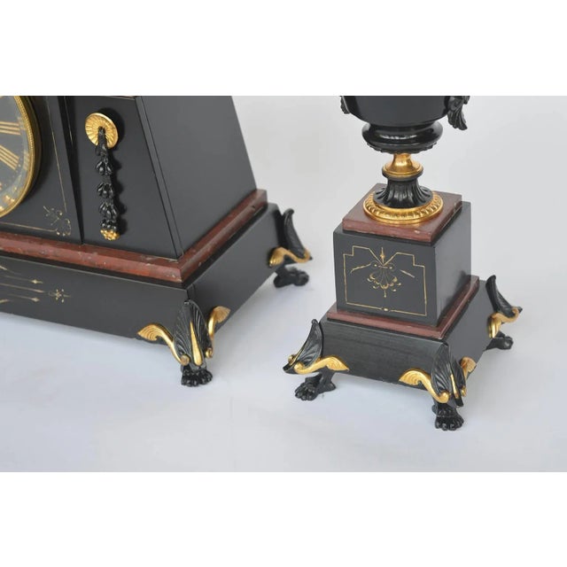 French bronze and marble Egyptian inspired clockset. Bronze with black patina. Measurements of urns: 13.5" H x 5.25" D x...