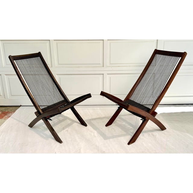This fantastic pair of vintage folding lounge chairs features a sculptural wood frame with woven black cord seat and back...