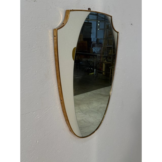 An Italian Mid Century shield-shaped wall mirror framed in slim brass, combining classic form with refined simplicity. The...