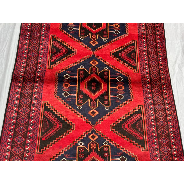 A striking vintage Afghan Baluchi rug featuring bold geometric diamond medallions in rich shades of red, navy, and dark...