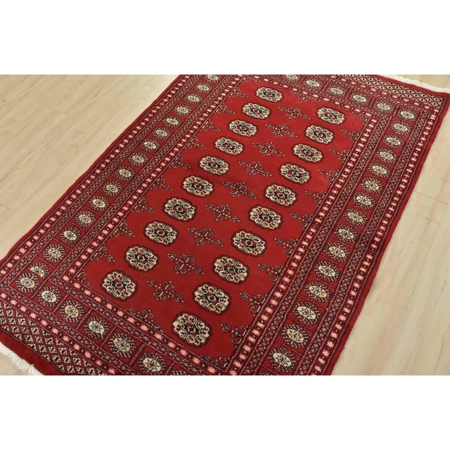 This tribal Bokhara rug is hand-knotted with an all-wool pile on a cotton foundation. This oriental rug features rows of...