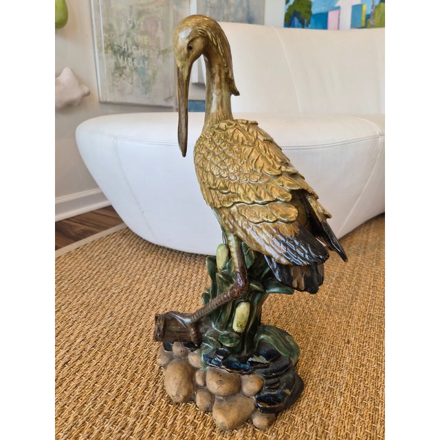 A clay sculpture of a spoonbill. It has many fine details and shows high craftsmanship. The Bird is resting on a bamboo...