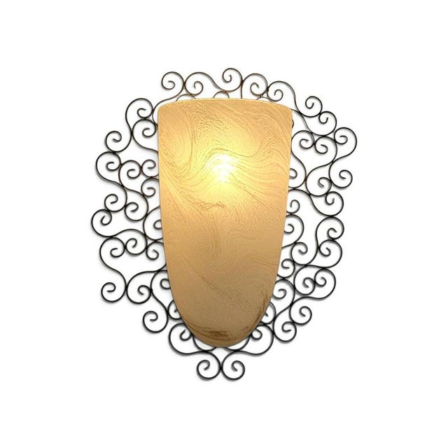 Wrought iron pocket wall sconces featuring a frosted amber glass shade nestled inside an intricate, black scrollwork metal...