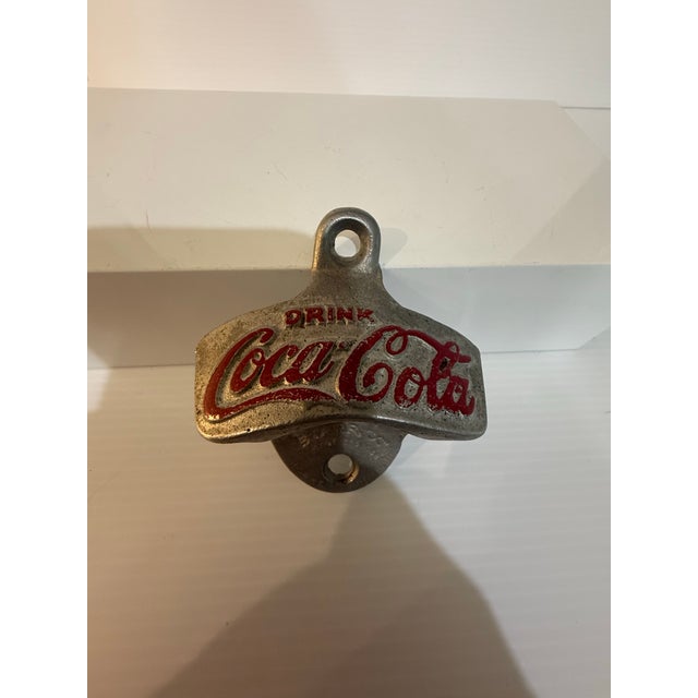 A classic vintage Coca-Cola “Drink Coca-Cola” STARR X wall-mounted bottle opener, rendered in cast metal with remnants of...