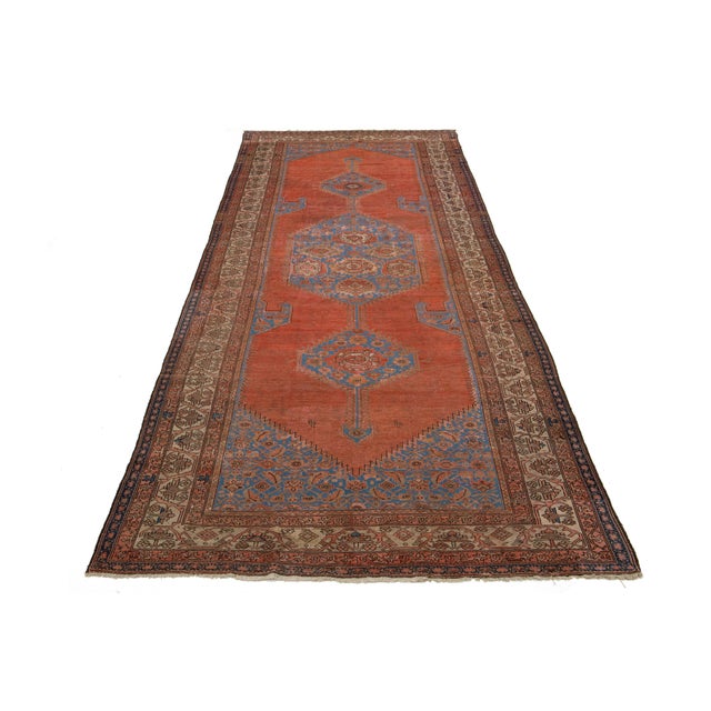 This hand-knotted antique Bakshaish runner features beige and blue accents on a vibrant rust background. These rugs are...