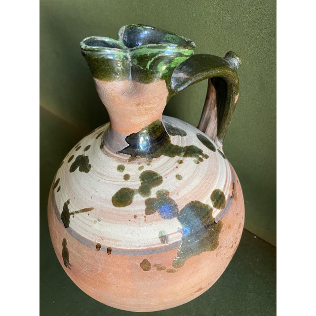 Country pottery terracotta jug with Fiancé color green splatter glaze and concentric circle design around the top of the...
