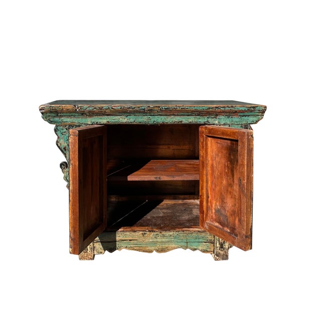 This is a low, antique-style wooden cabinet with a heavily distressed, rustic finish. The cabinet is coated in a faded...